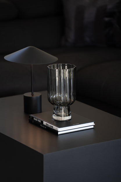 Geriffelte graue Glasvase auf Buch als elegante moderne Tischdekoration neben minimalistischer Tischlampe