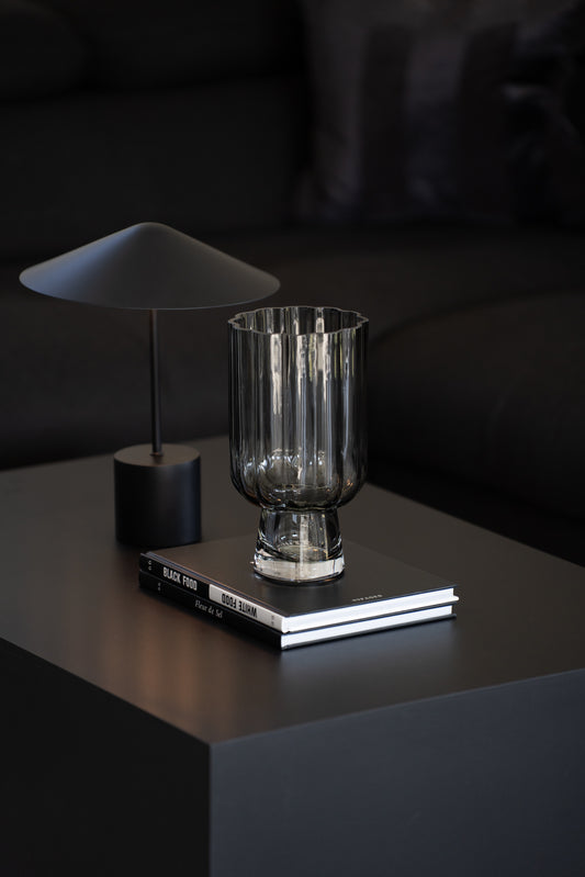 Geriffelte graue Glasvase auf Buch als elegante moderne Tischdekoration neben minimalistischer Tischlampe