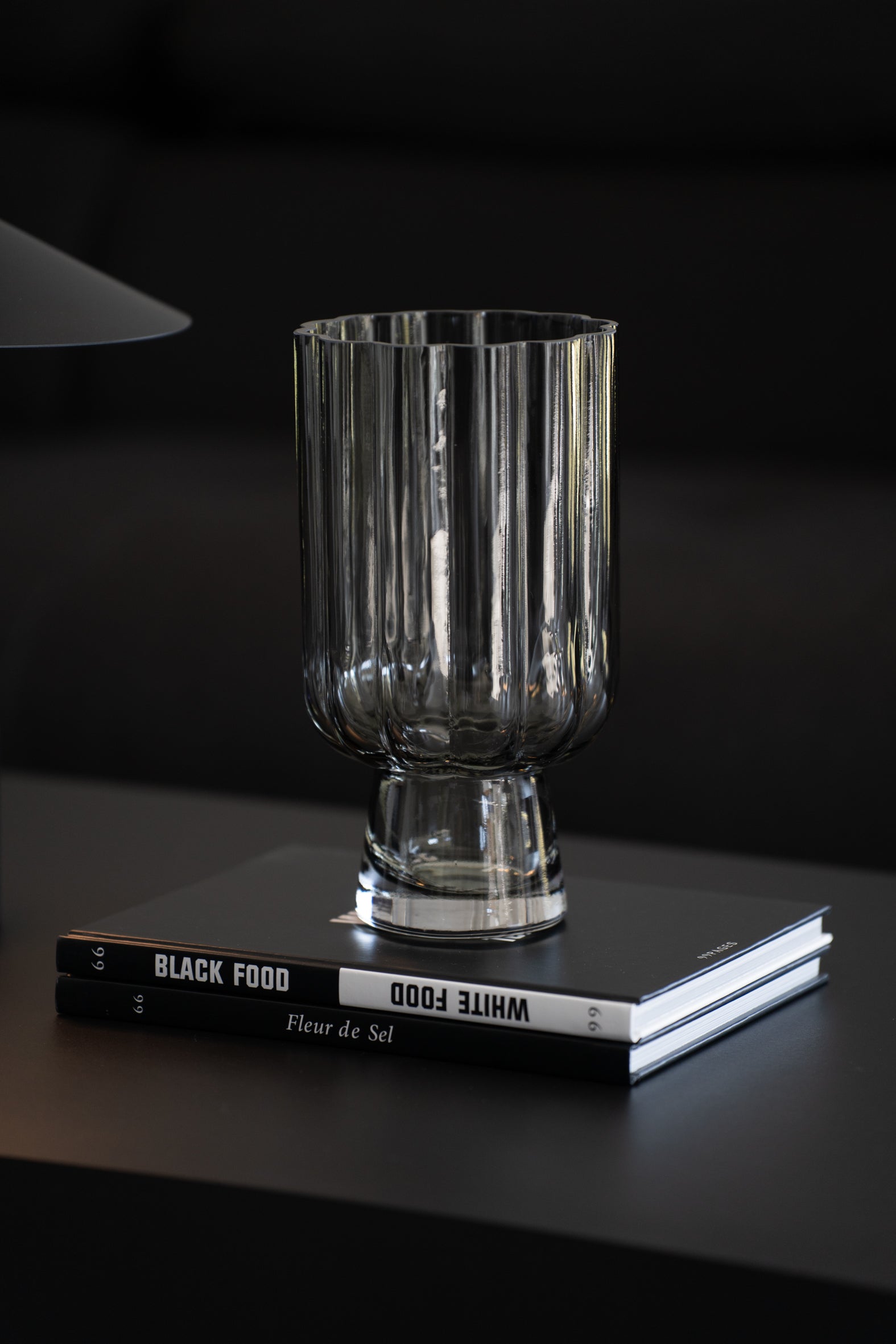 Geriffelte graue Glasvase auf Buch als elegante moderne Tischdekoration neben minimalistischer Tischlampe