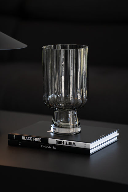 Geriffelte graue Glasvase auf Buch als elegante moderne Tischdekoration neben minimalistischer Tischlampe