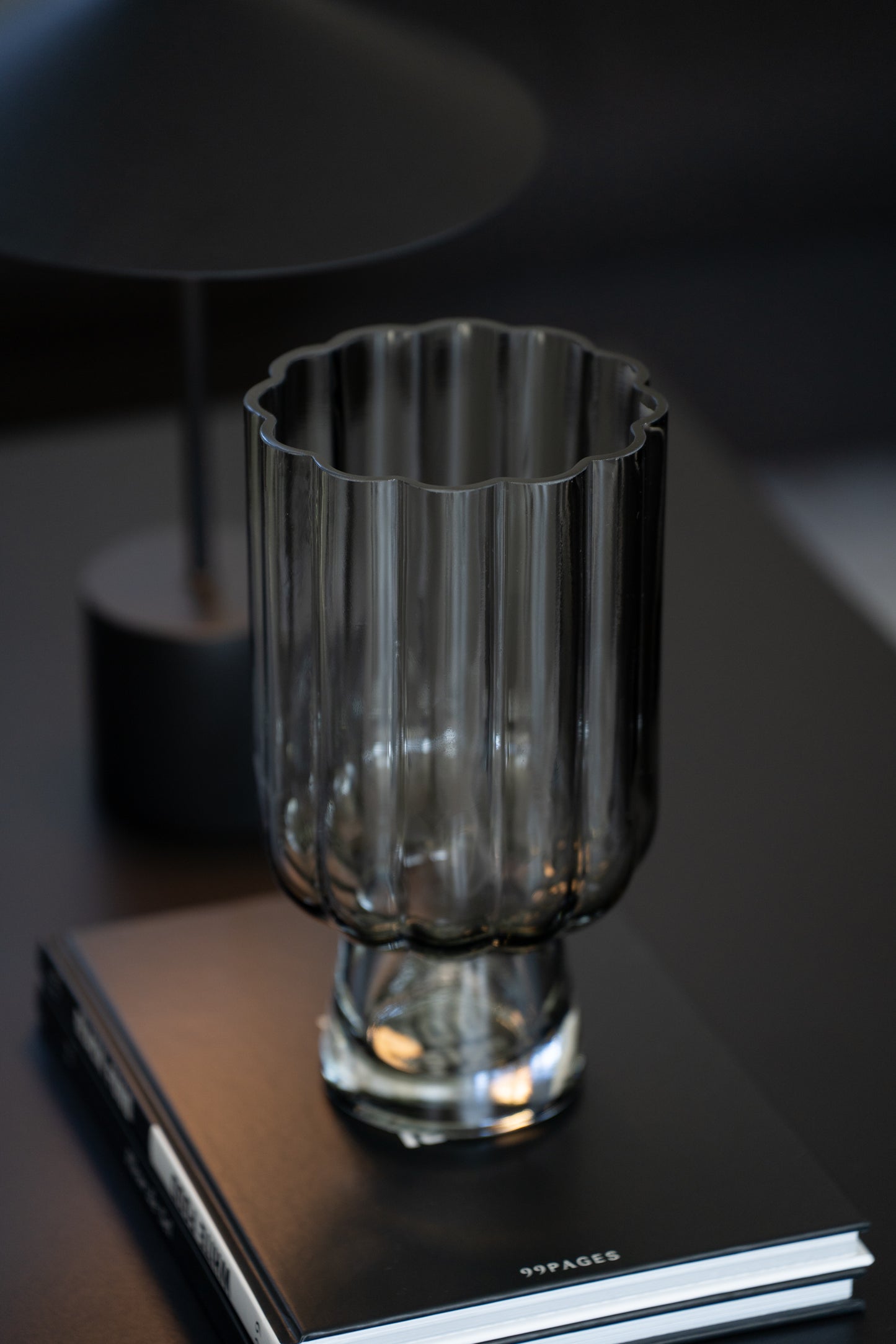 Geriffelte graue Glasvase auf Buch als elegante moderne Tischdekoration neben minimalistischer Tischlampe