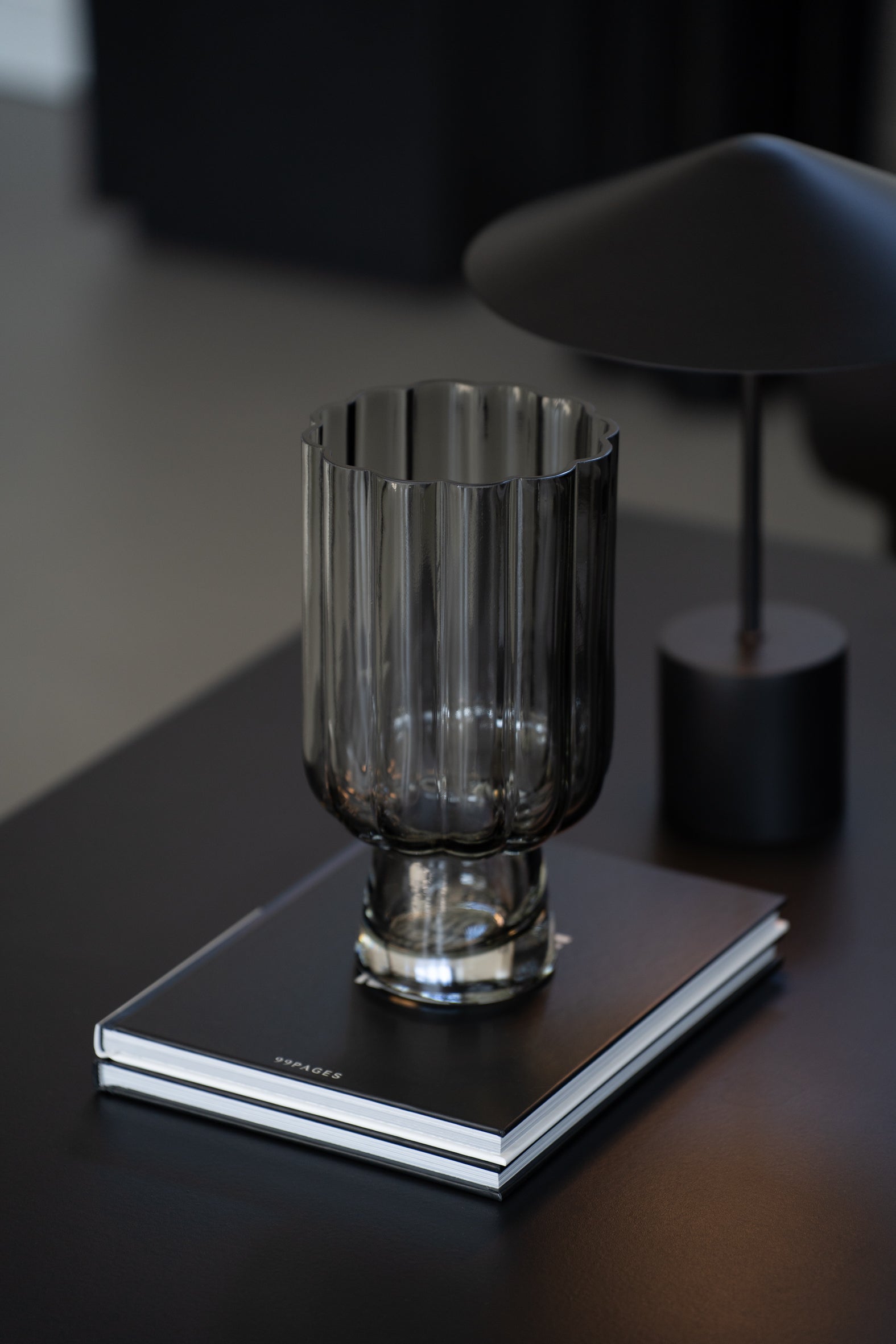 Geriffelte graue Glasvase auf Buch als elegante moderne Tischdekoration neben minimalistischer Tischlampe