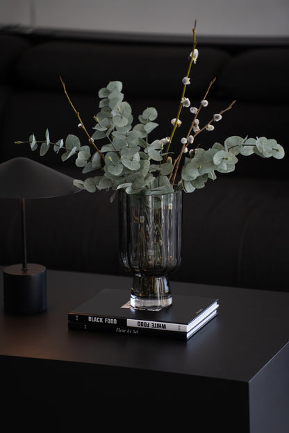 Geriffelte graue Glasvase auf Buch als elegante moderne Tischdekoration neben minimalistischer Tischlampe