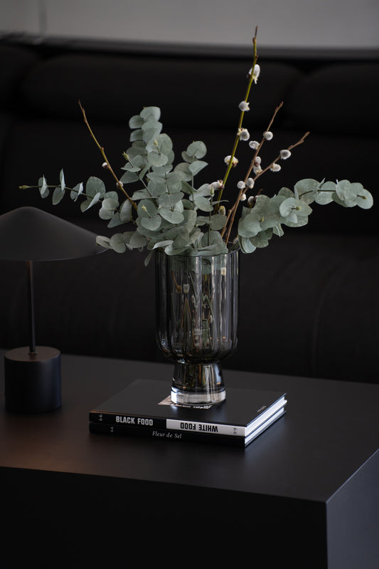 Geriffelte graue Glasvase auf Buch als elegante moderne Tischdekoration neben minimalistischer Tischlampe