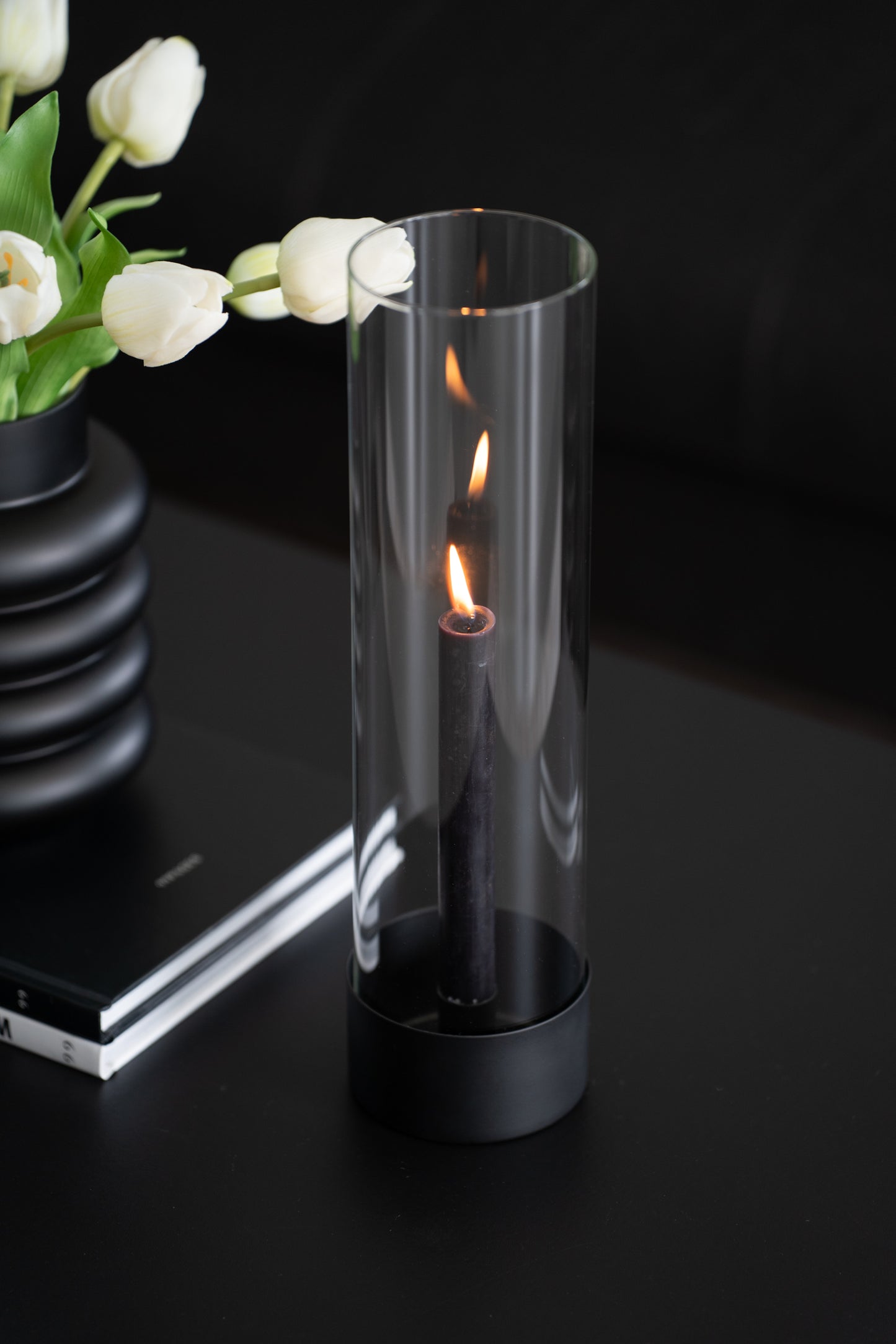 Stabkerzenhalter mit schwarzem Sockel und Glaszylinder im modernen minimalistischen Design - Beispiel mit brennender Kerze